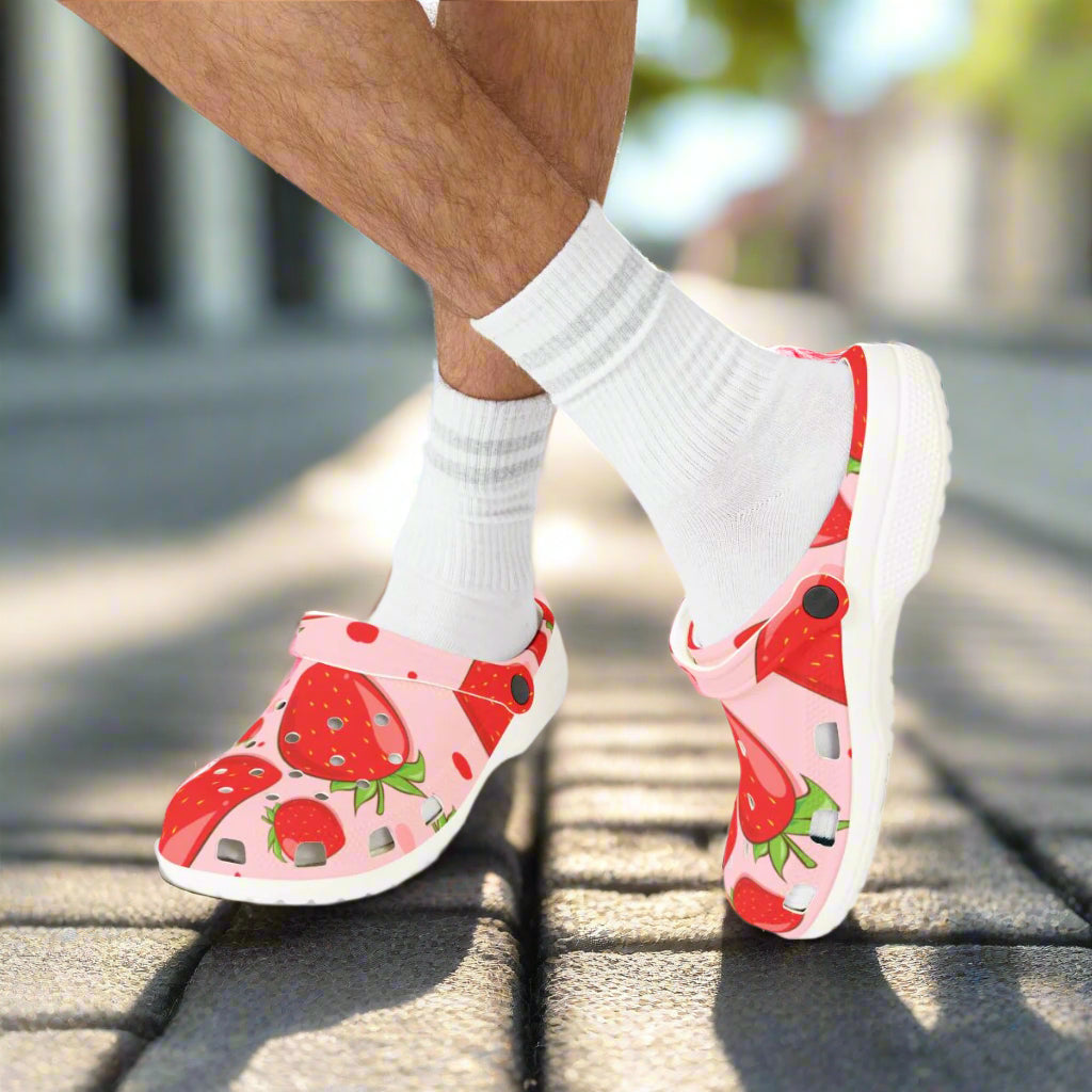 Pink clogs with strawberry design worn with white socks on a white background