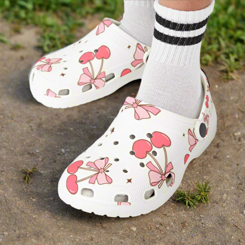 White clogs with pink floral design worn by a child on a white background
