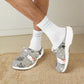 Gray clogs with cat design worn with white socks on a white background