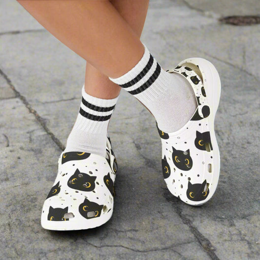 White slip-on shoes with black cat patterns worn with white socks on a white background
