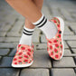 Pink slip-on shoes with strawberry pattern worn with white socks on a white background
