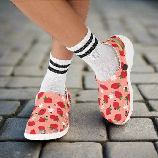 Pink slip-on shoes with strawberry pattern worn with white socks on a white background